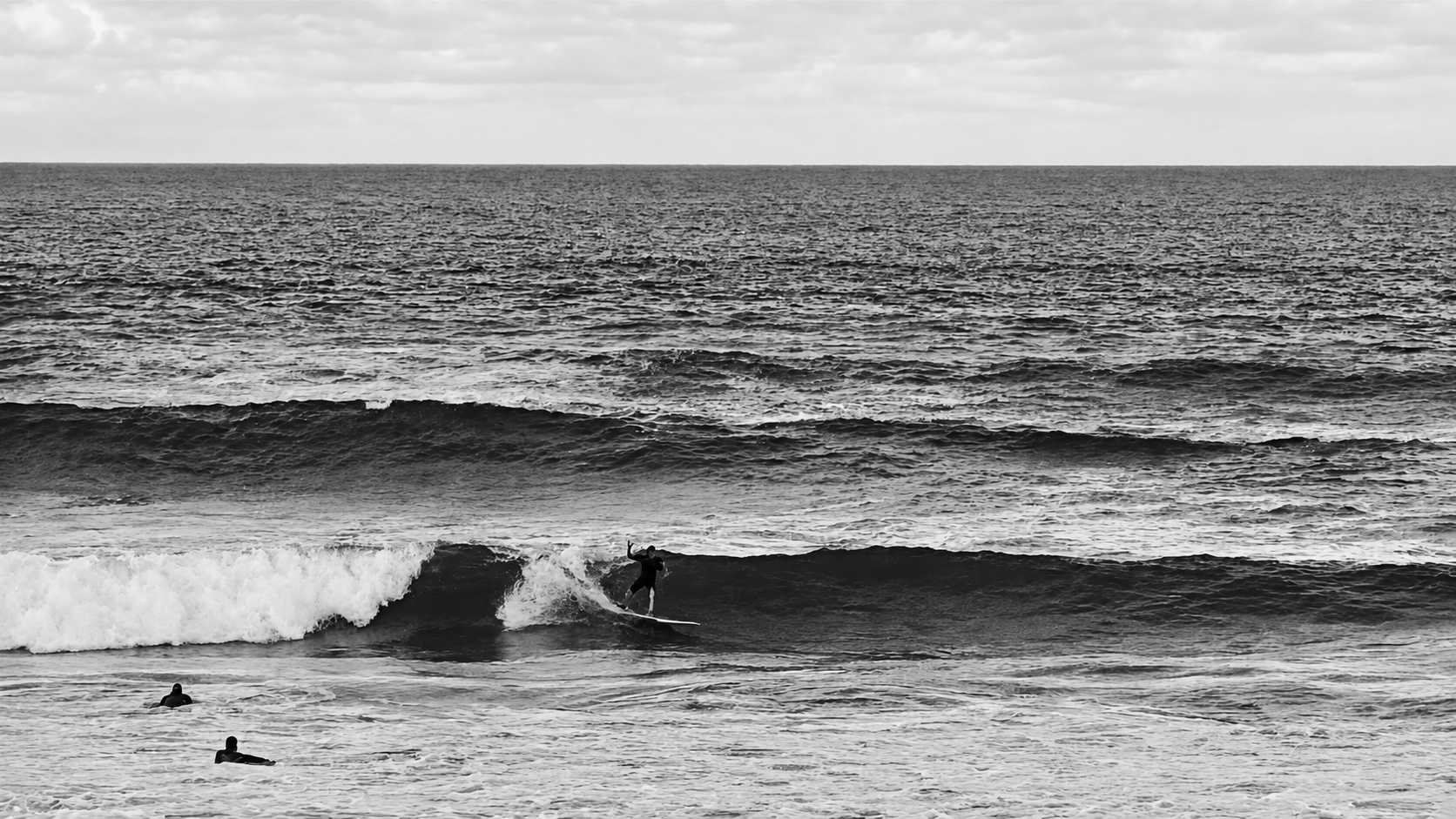 Surfista em uma onda com outros surfistas no mar, fotografia em preto e branco