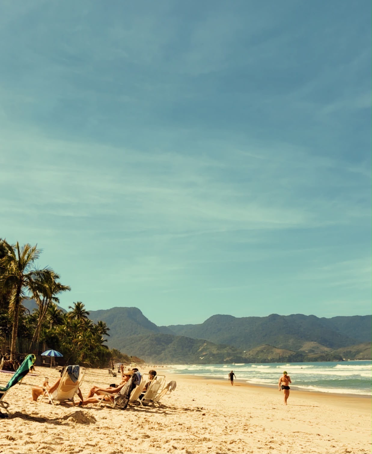 Praia com palmeiras, montanhas e mar azul